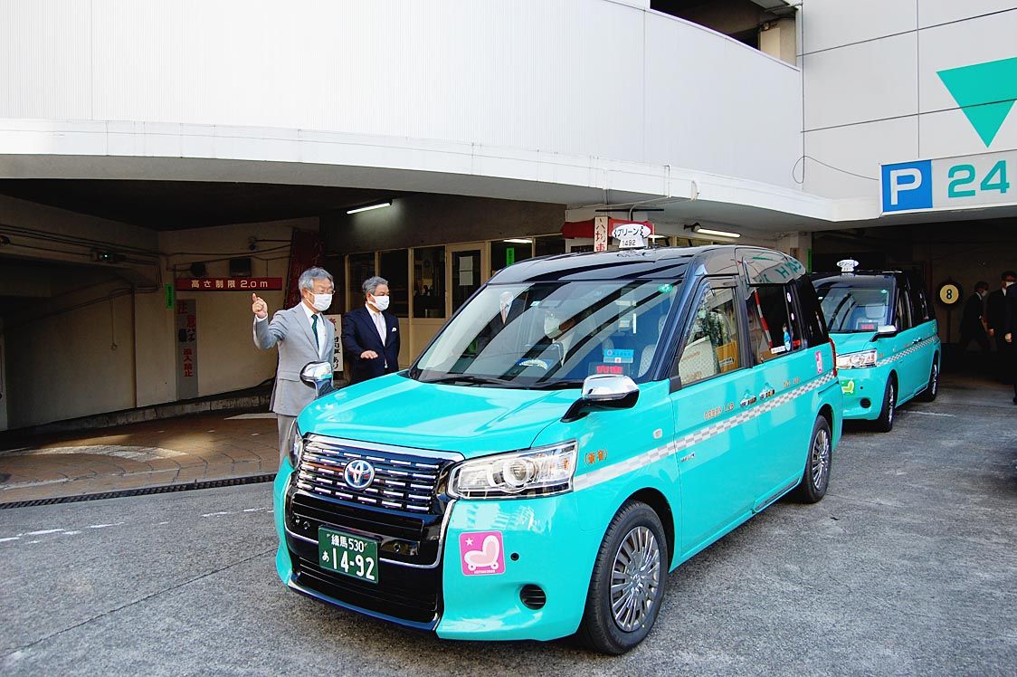 出発する新色車両を見送る髙野社長(左)