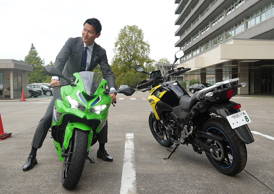 各社のバイクにまたがる朝日副大臣。バイク免許は持っていないが、四輪車の希望ナンバーを取得しているという