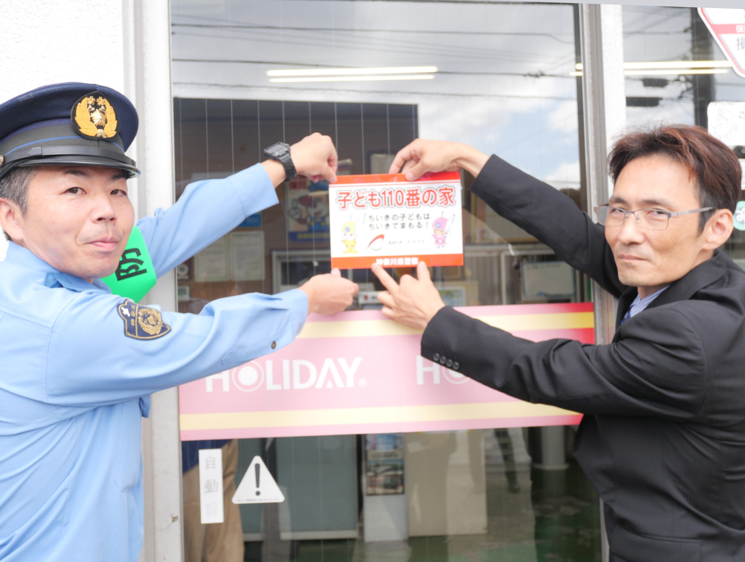 店舗入り口にステッカーを貼付する本川博ブロック長(右)と鮫嶋哲郎警部補